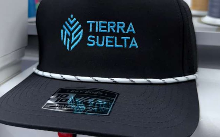 A finished cap with an embroidered brand logo, thread cones in the shop behind